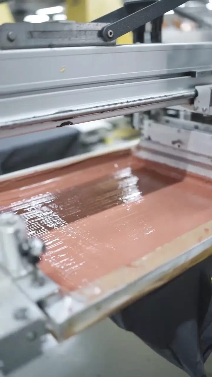 Close-up of a polyurethane squeegee blade flooding custom colored ink through a printing mesh