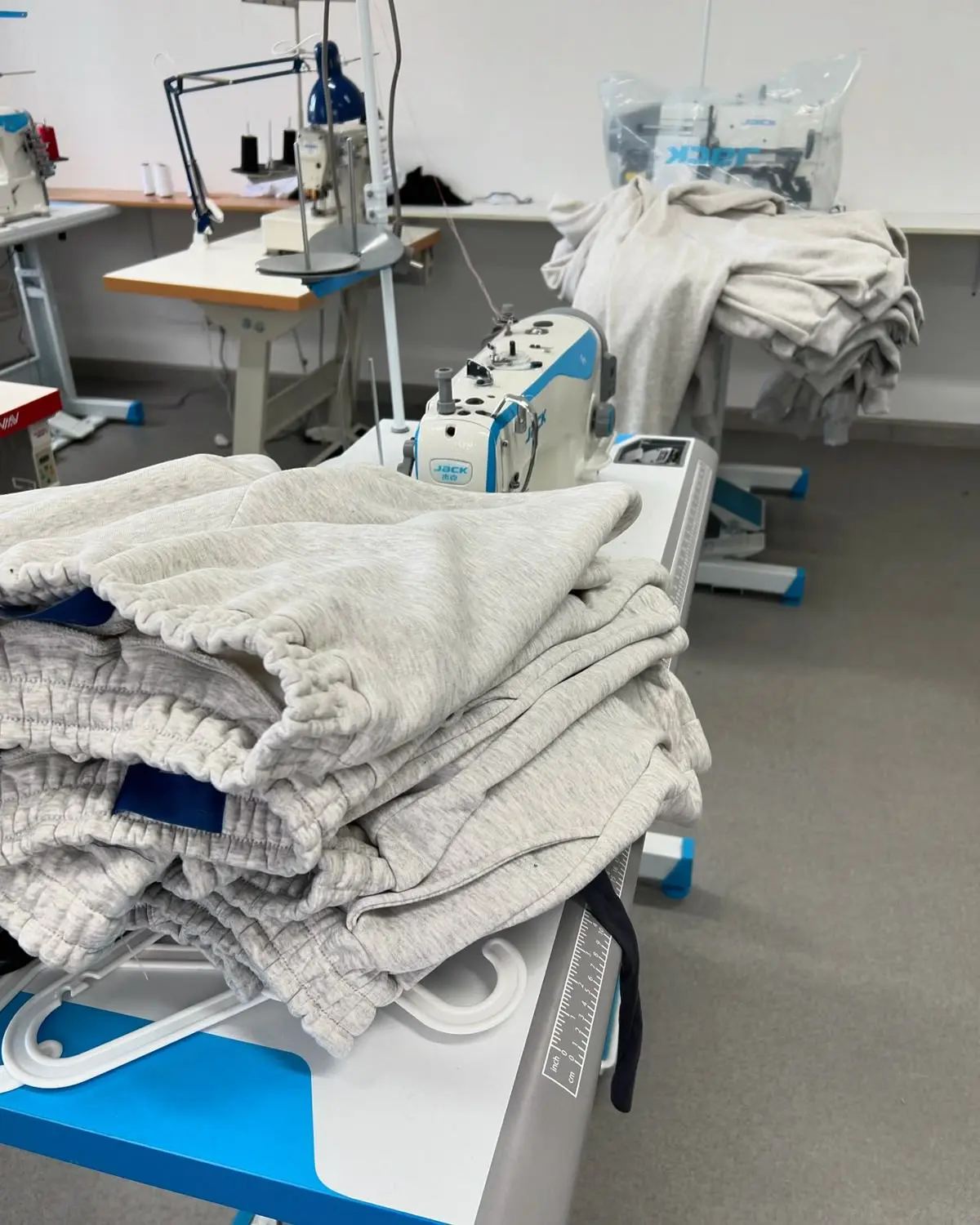 A pair of freshly assembled fleece streetwear sweatpants laid flat across an industrial stitching bench