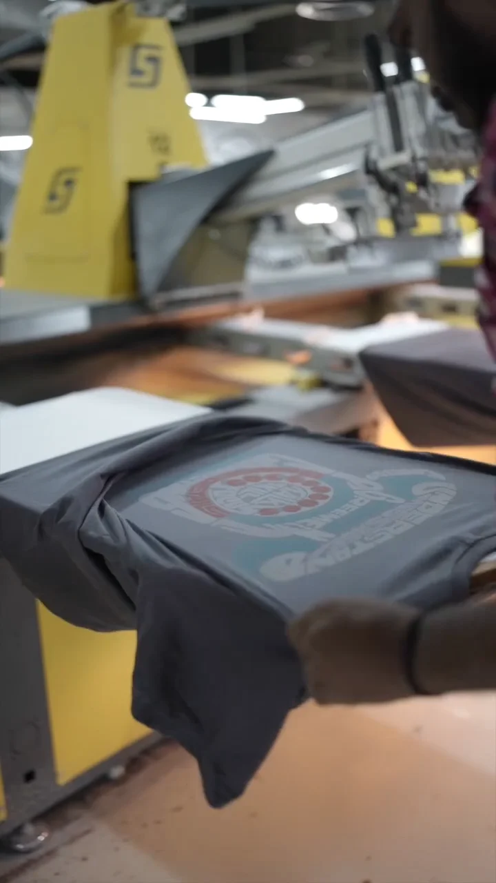 A skilled screen printer applying graphic ink layers to a custom blank t-shirt panels